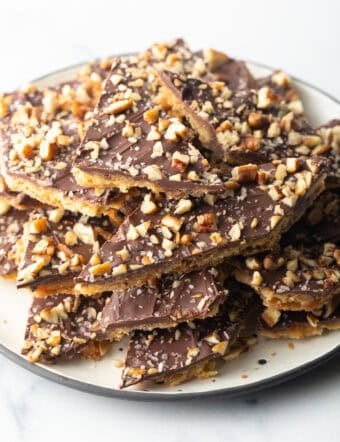 Pieces of salted toffee and chocolate candy aka Christmas crack piled up and stacked on a white plate.