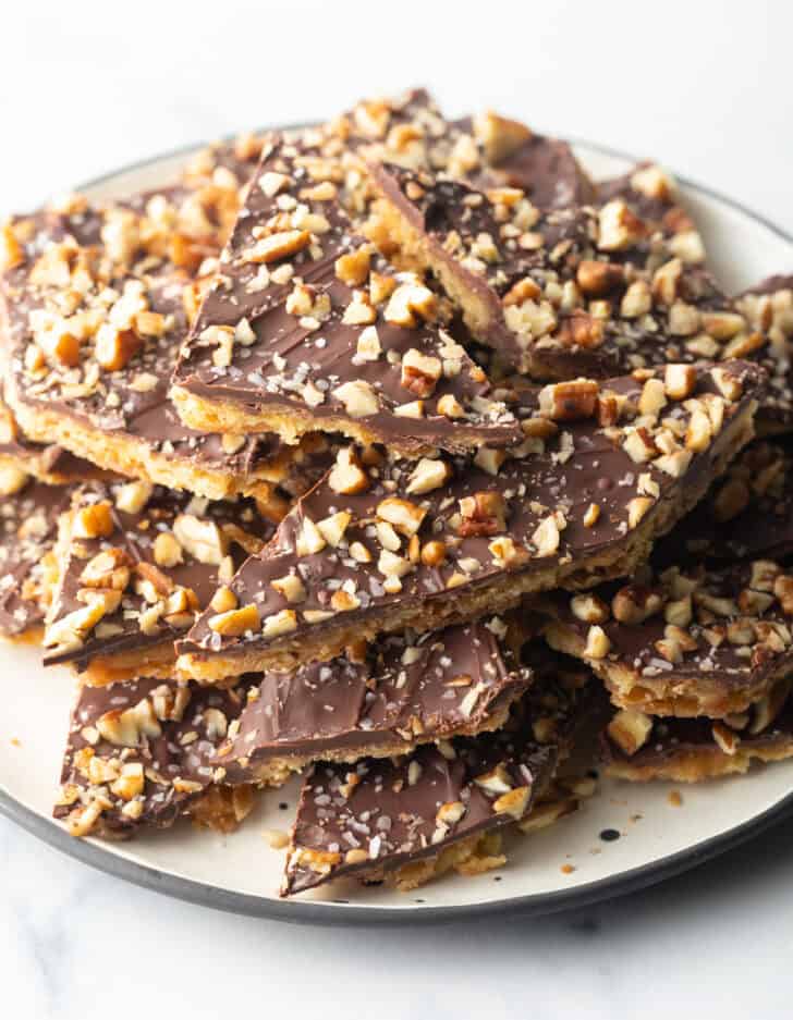 Pieces of salted toffee and chocolate candy aka Christmas crack piled up and stacked on a white plate.