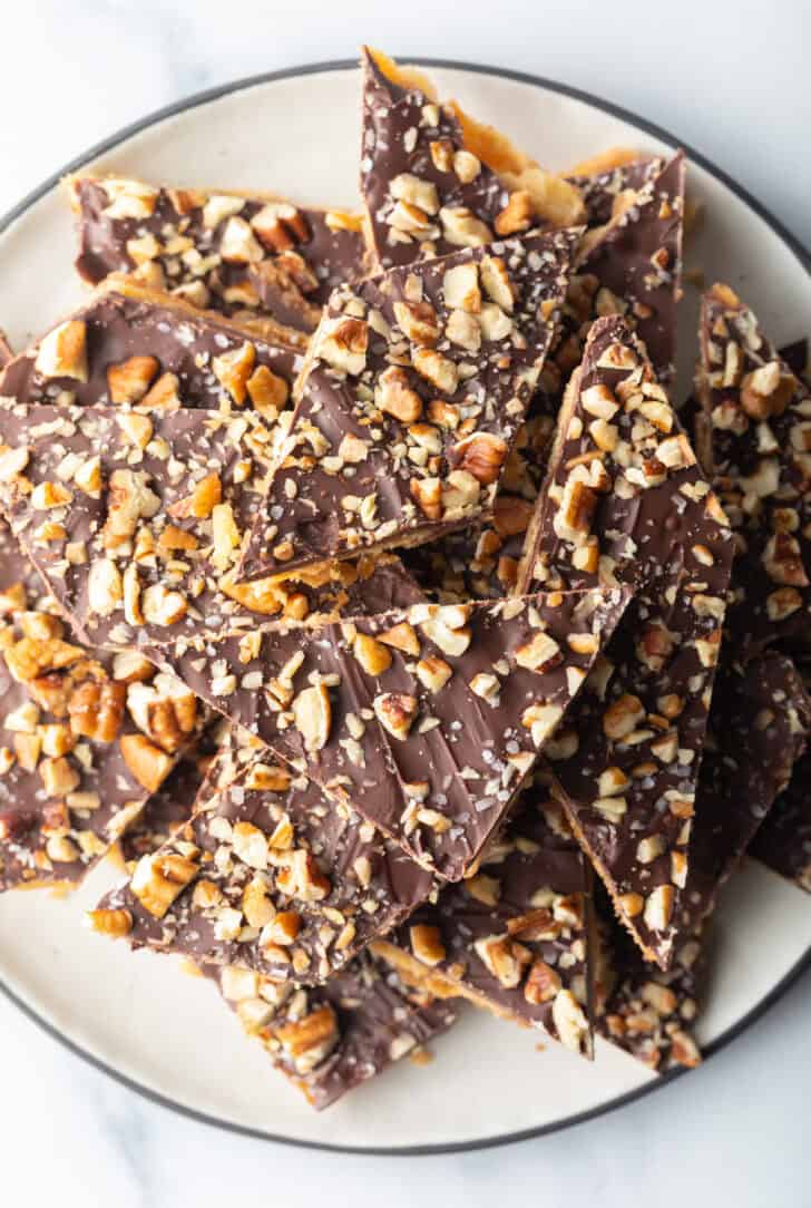 Overhead view pieces of salted toffee and chocolate candy piled up and stacked on a white plate.