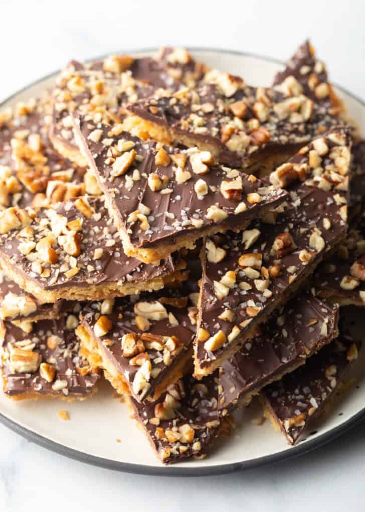 Overhead view pieces of salted toffee and chocolate candy aka Christmas crack piled up and stacked on a white plate.