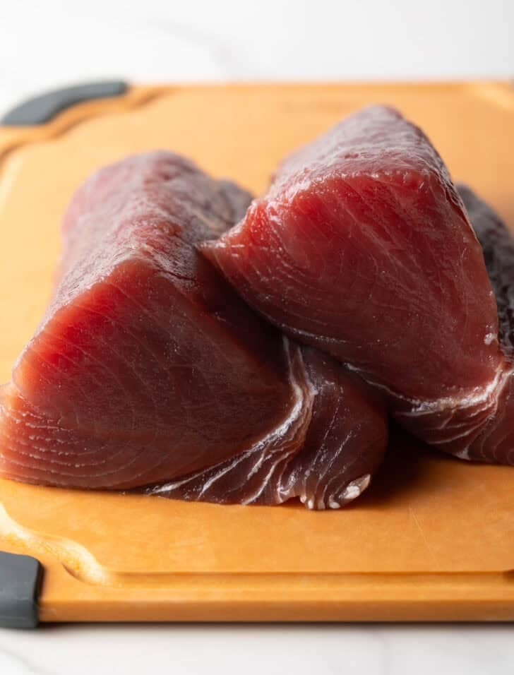 Two large pieces of raw yellowfin tuna on a cutting board.
