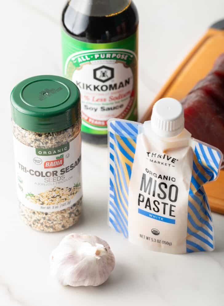Yellowfin marinade ingredients: Jar of tricolor sesame seeds, bottle of soy sauce, whole bulb of garlic, and squeeze pack of miso paste.