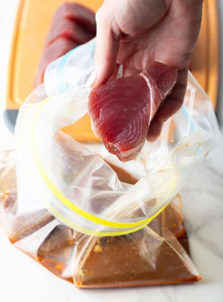 Hand adding slices of yellowfin tuna to a plastic bag with marinade.
