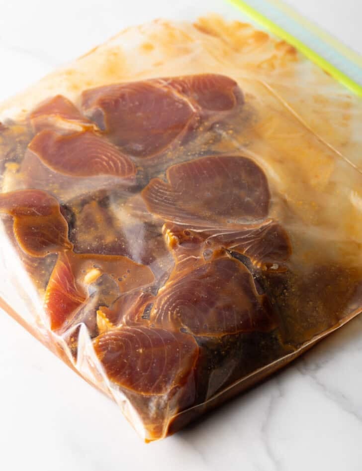 Several tuna steaks marinating in a ziploc bag.
