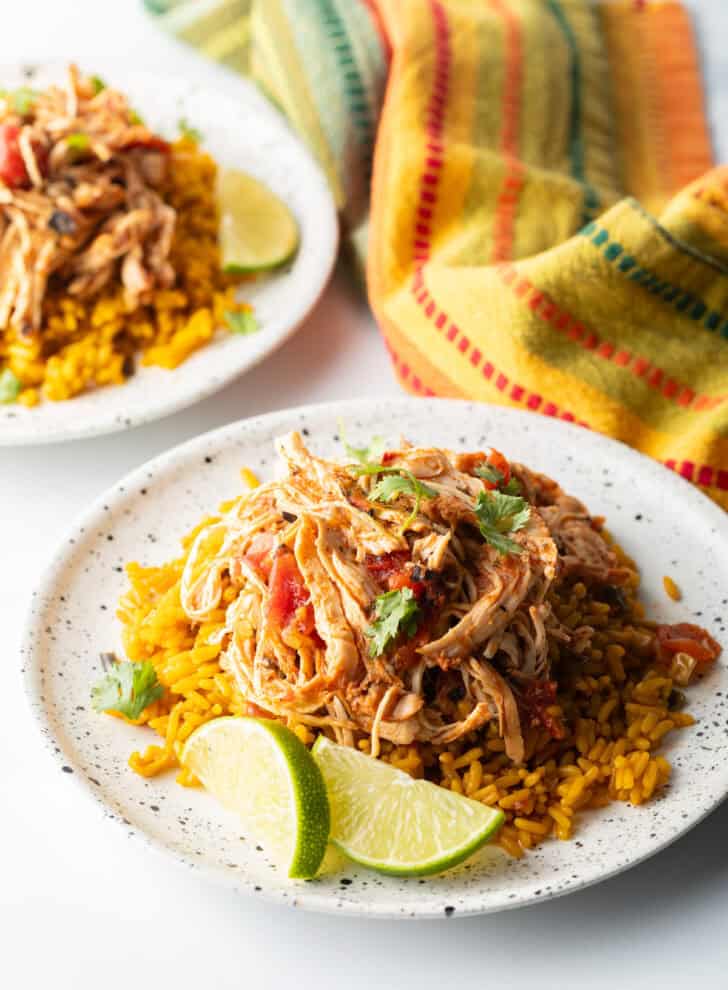 Mound of zesty shredded Mexican chicken on a plate with spanish rice and lime wedges.