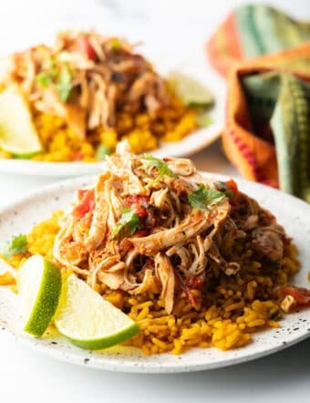 Mound of zesty shredded Mexican chicken on a plate with spanish rice and lime wedges.