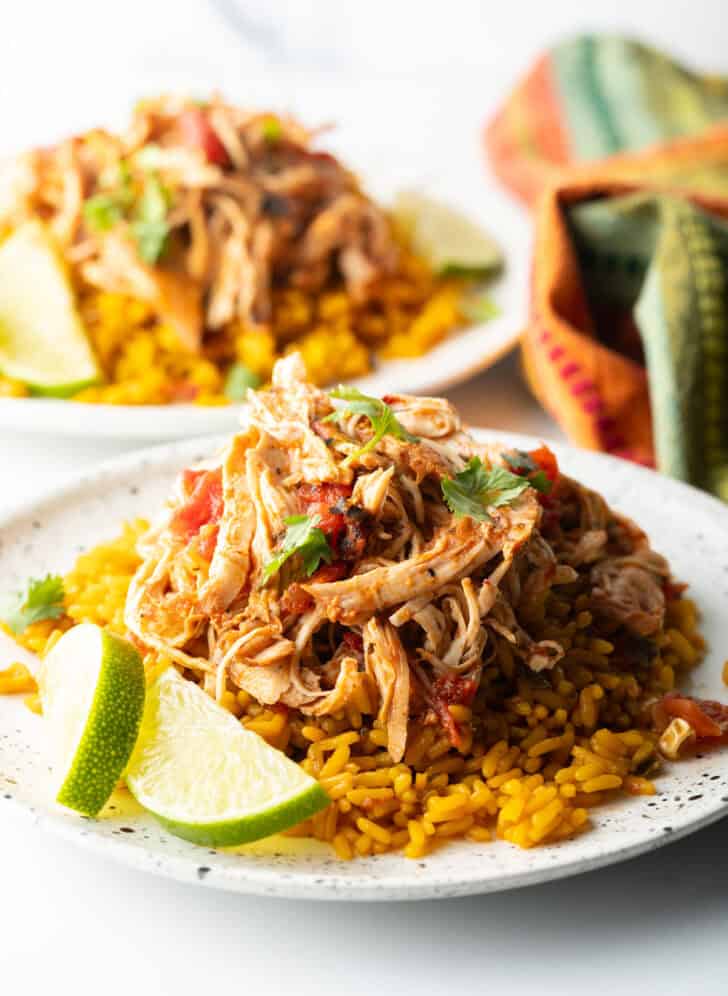 Mound of zesty shredded Mexican chicken on a plate with spanish rice and lime wedges.