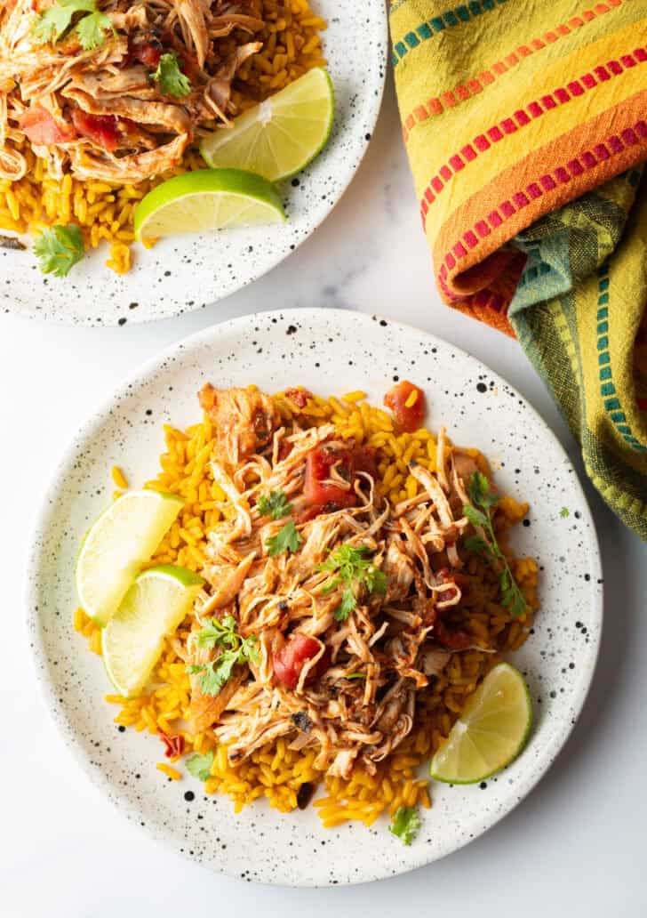 Top down view mound of zesty shredded Mexican chicken on a plate with spanish rice and lime wedges.