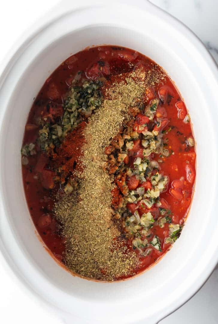 Top down view white crock pot with salsa and cooked herbs.