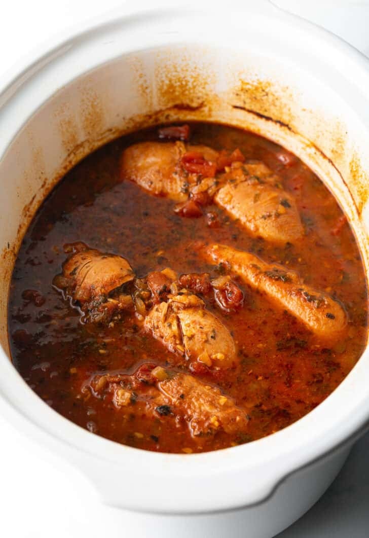 Several whole chicken breasts covered in red sauce in a white crockpot.