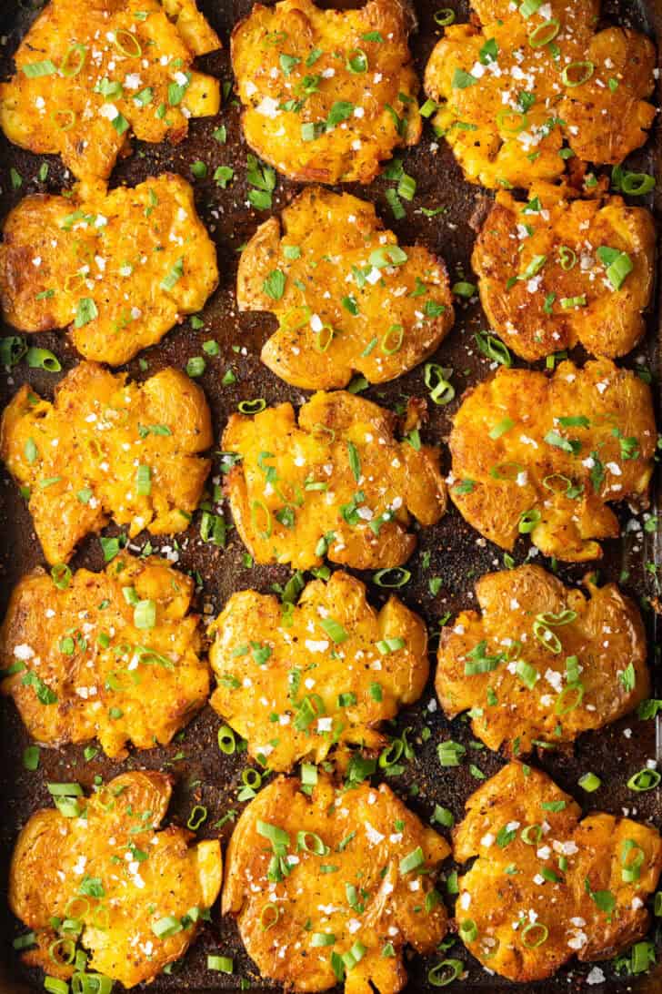 Top down view of 15 golden smashed potatoes on a baking sheet.