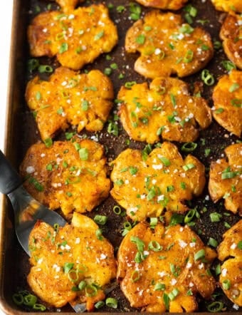 Top down view of 15 golden smashed potatoes on a baking sheet.