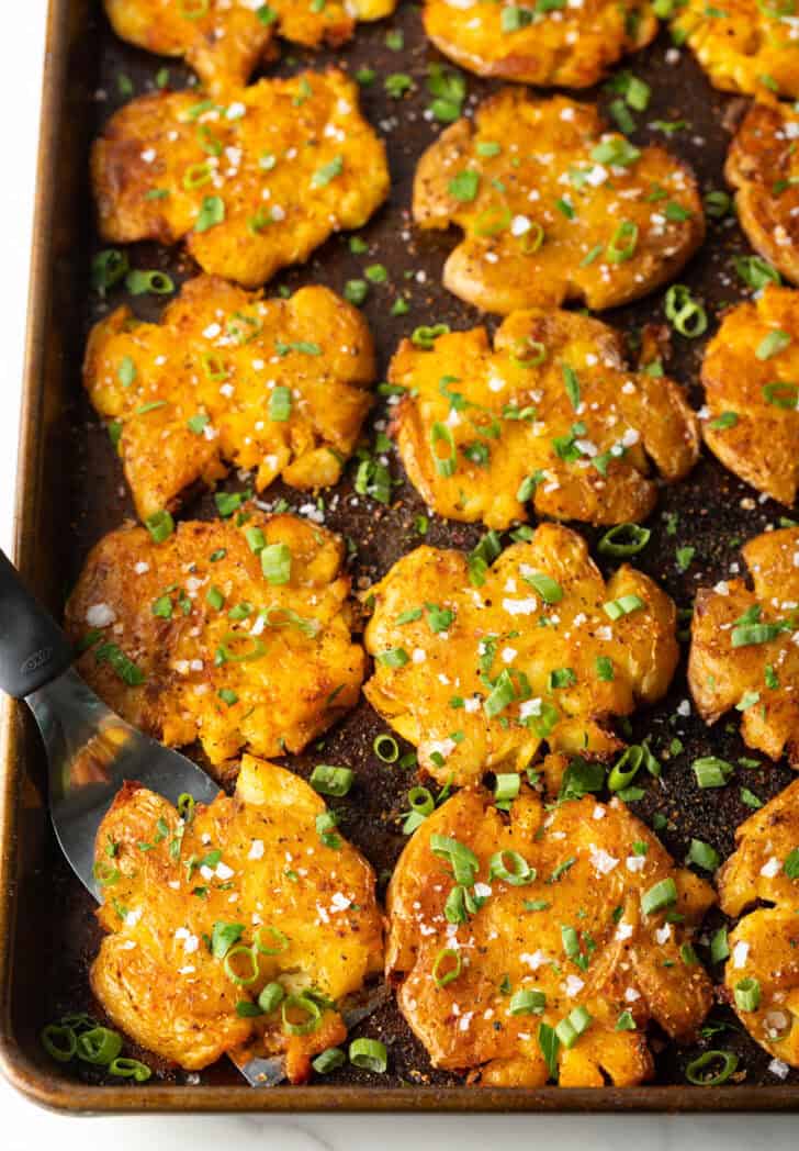 Top down view of 15 golden smashed potatoes on a baking sheet.