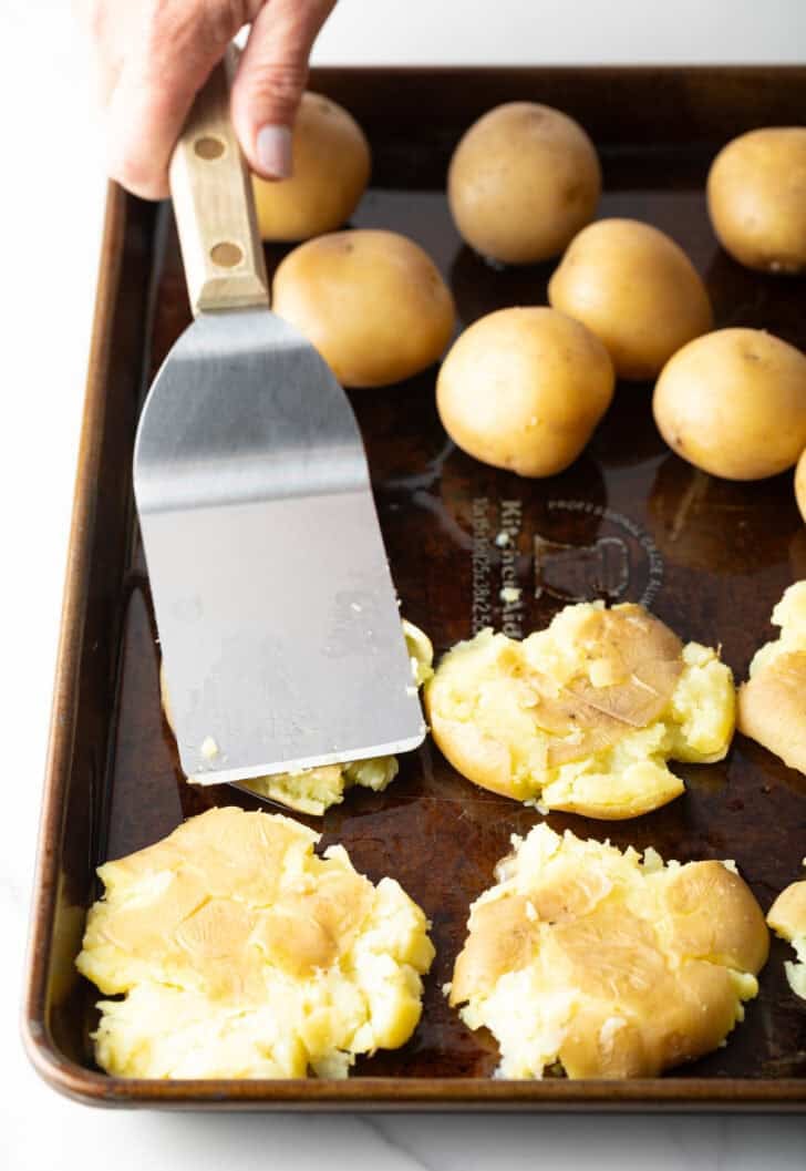 Using a metal spatula to smoosh small unbaked yellow potatoes.