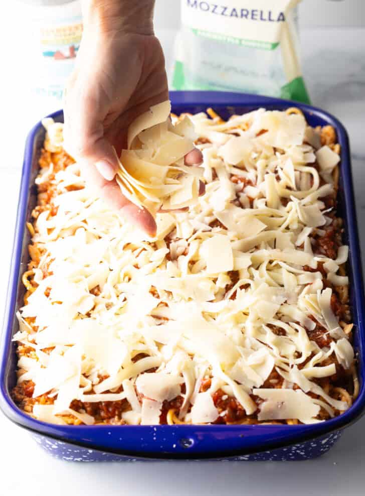 Hand adding shredded parmesan cheese on top of spaghetti casserole.