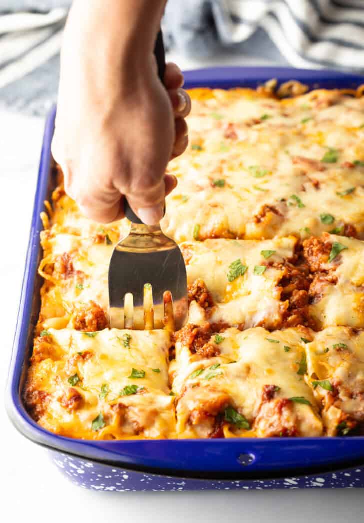 Using a metal spatula to cut spaghetti casserole into 12 pieces.
