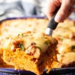 Hand with a spatula holding a serving of baked spaghetti to camera.