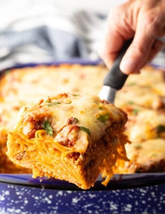Hand with a spatula holding a serving of baked spaghetti to camera.