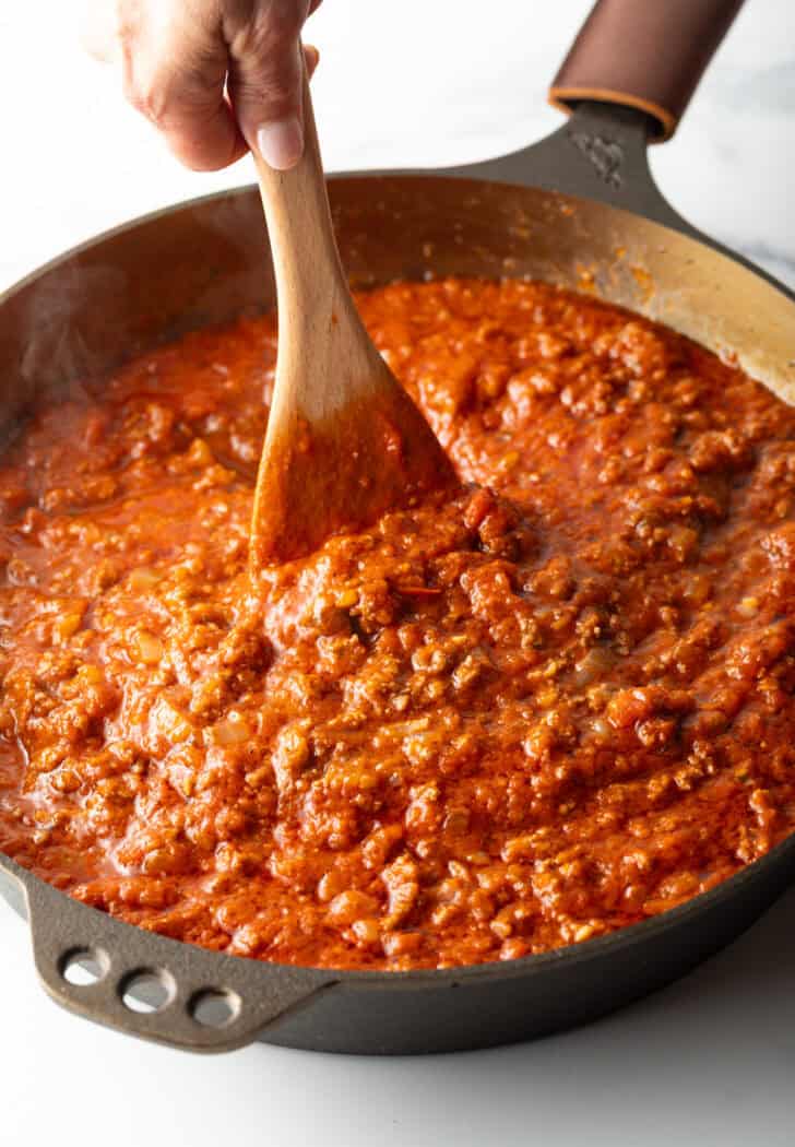 Stirring meat pasta sauce with a wooden spatula.