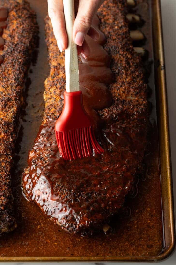 St Louis-style ribs on oven tray being brushed with barbecue sauce.