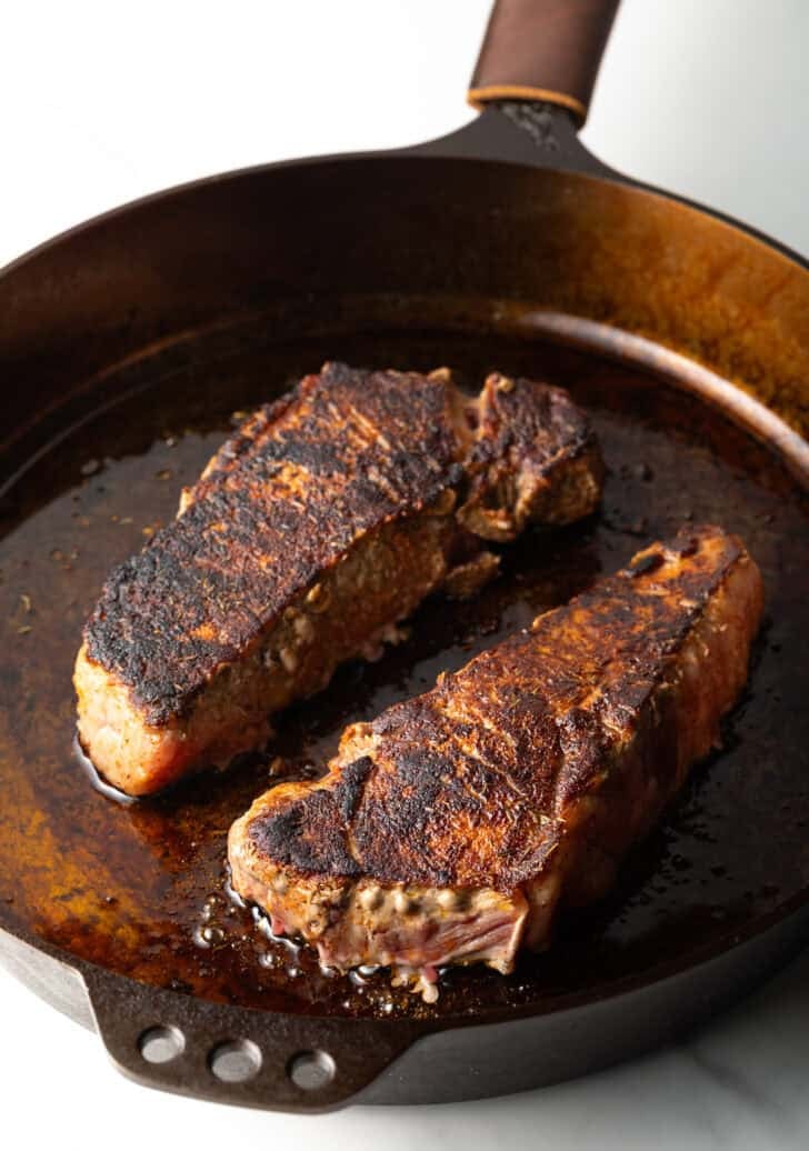Two seared ribeye steaks in a cast iron.