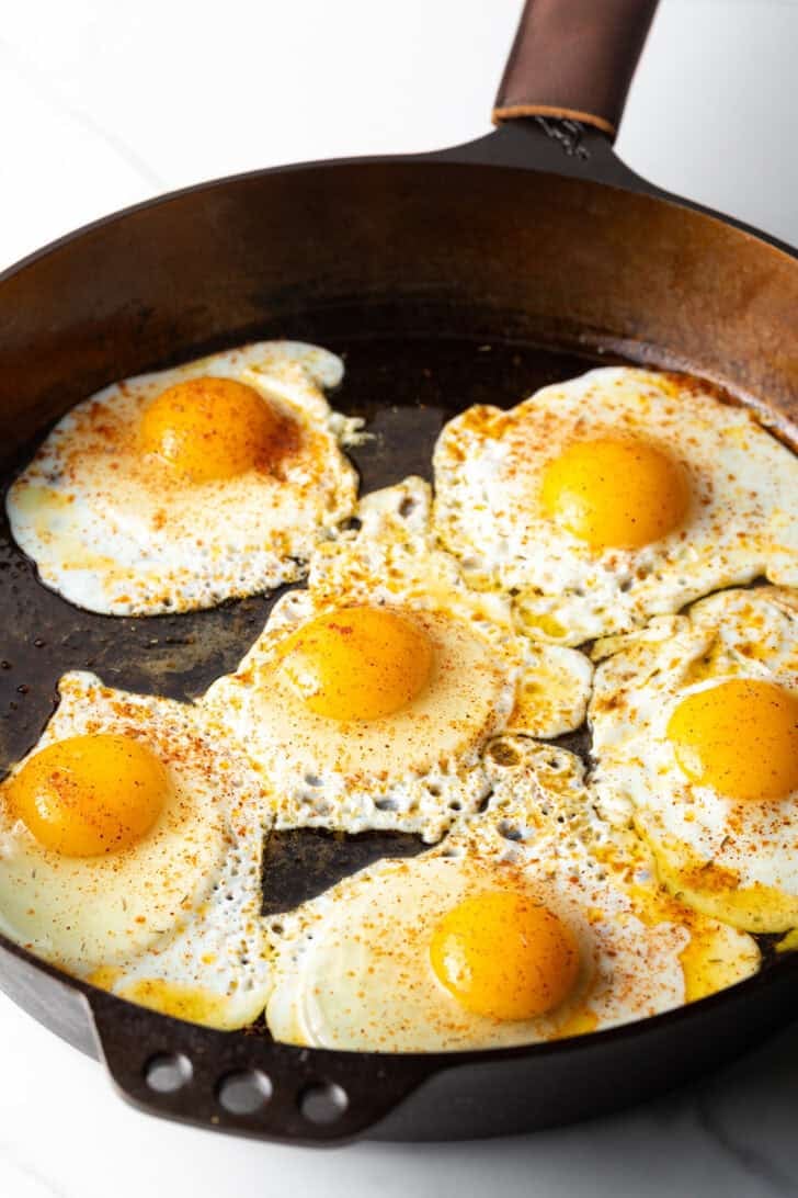 6 sunny side up fried eggs in a cast iron pan.