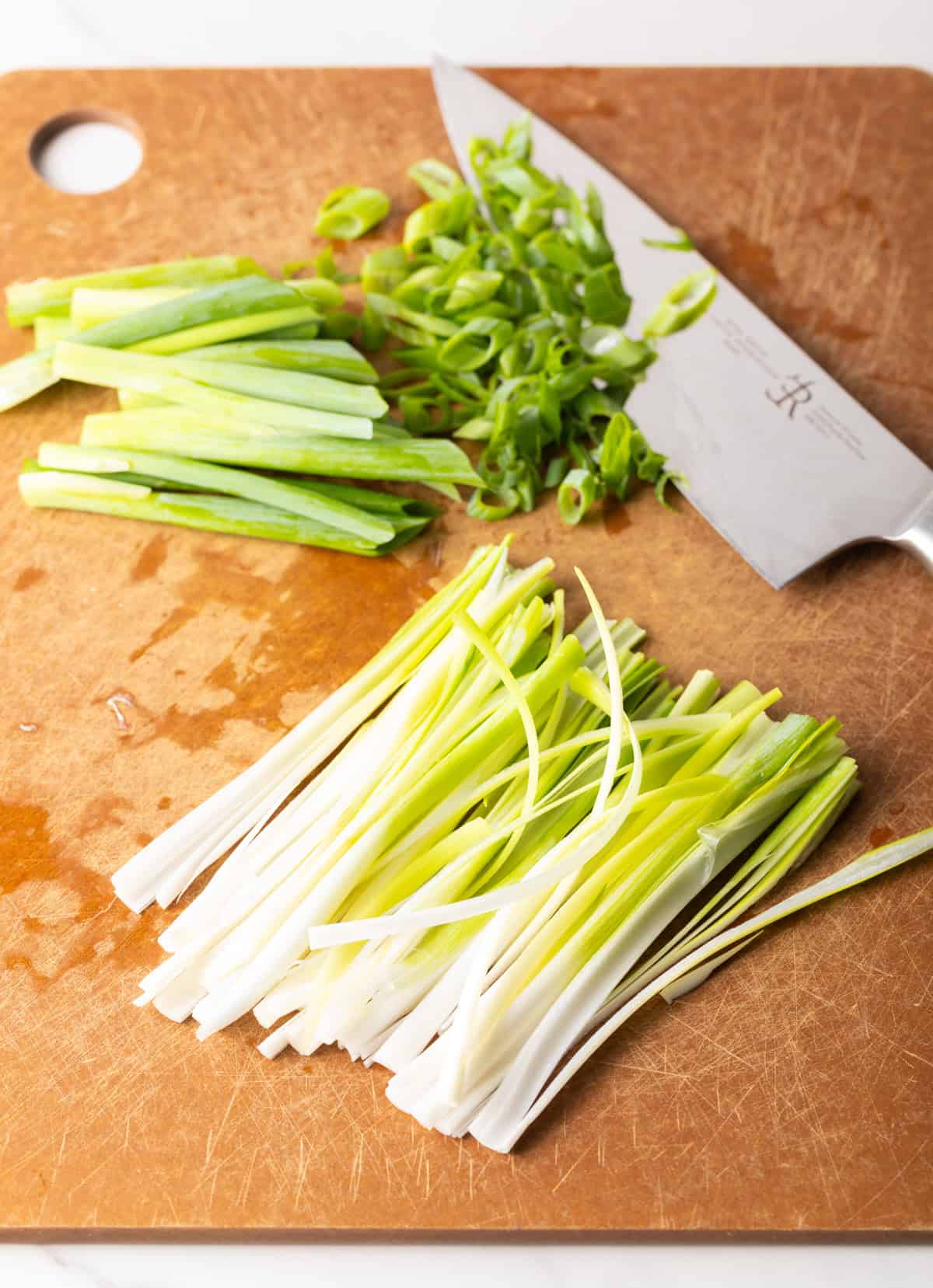 Chopped green onions on a cutting board next to a knife.