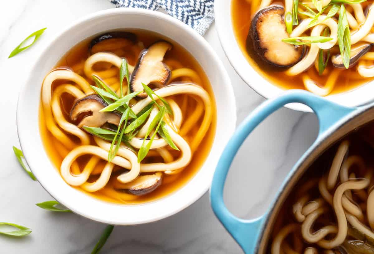 Overhead view of udon soup recipe in two white bowls next to pot of soup.