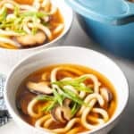 Easy udon noodle soup in 2 white bowls next to a pot of soup.