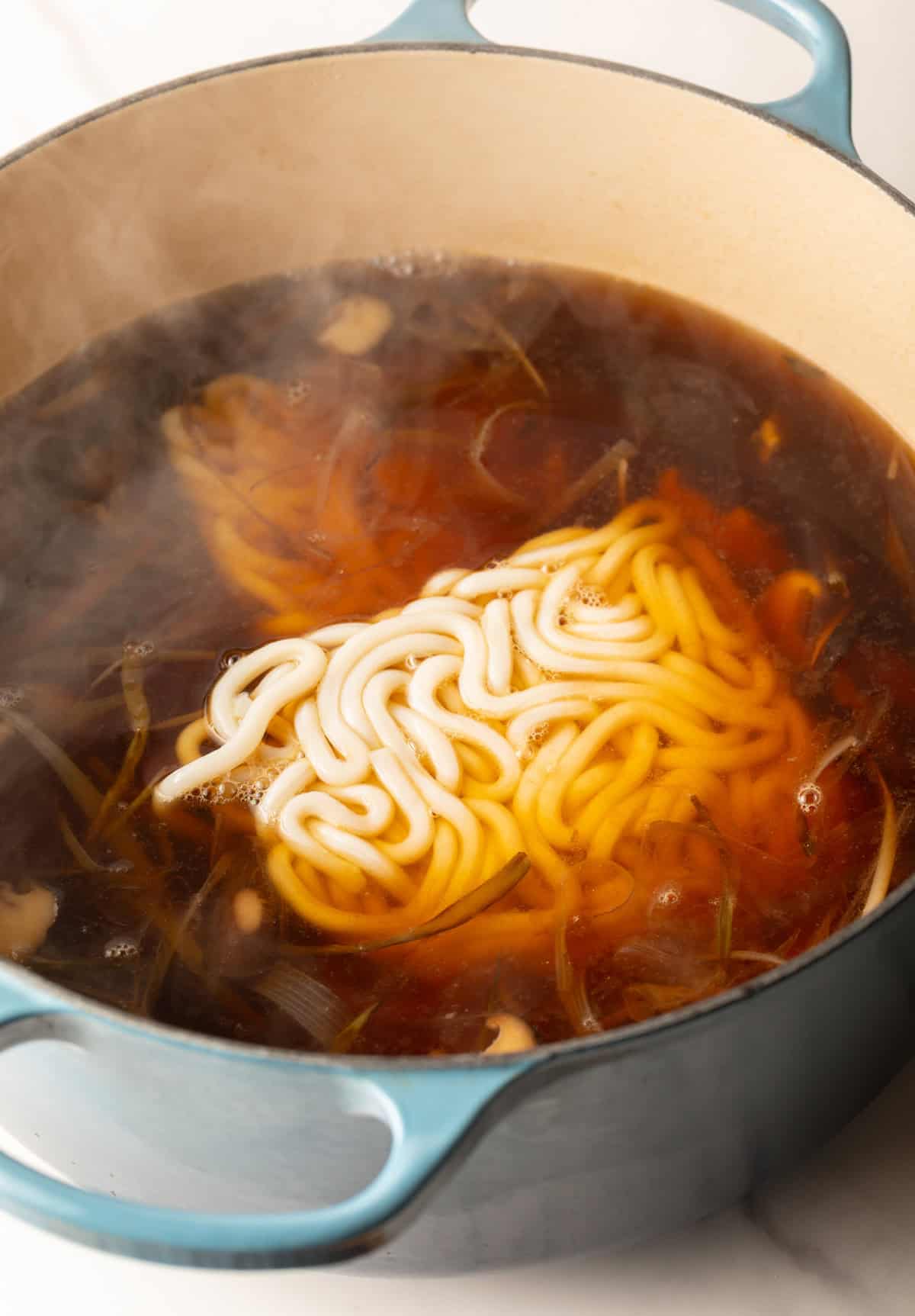 Udon noodles being added to the udon noodle soup broth in a pot.