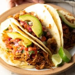 Hand holding Crockpot Carnitas in tacos on plate