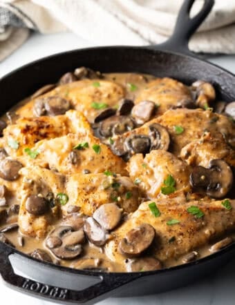 Mushroom Chicken - Cast iron brimming with seared chicken breast pieces and sliced mushrooms in a brown gravy.