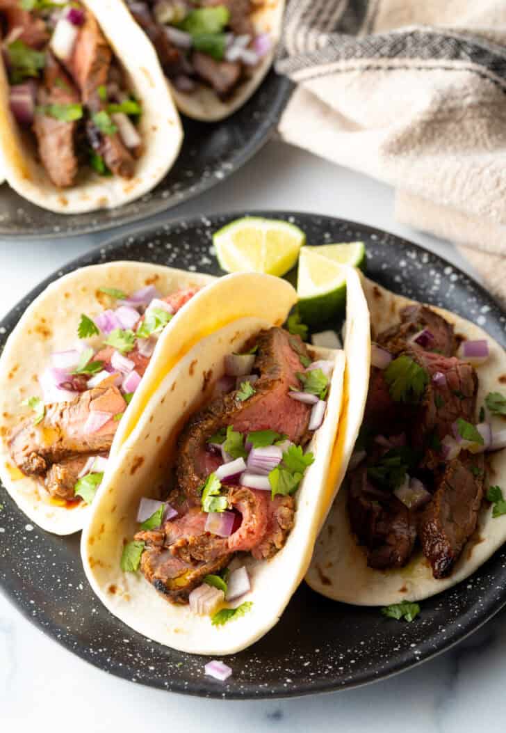 3 tacos on a black plate.