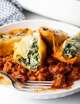 Four stuffed shells with spinach and meat sauce on a white plate.