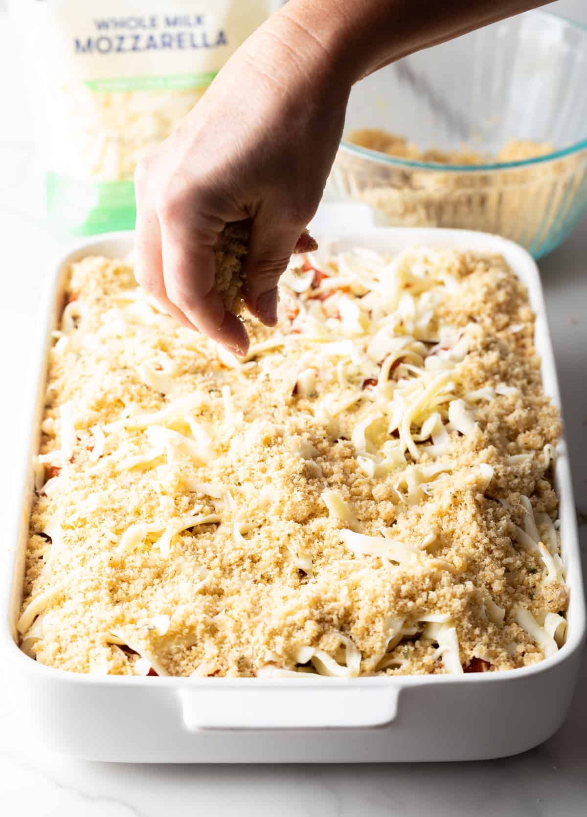 A mozzarella cheese and breadcrumb mixture is being added to the chicken parmesan casserole recipe.