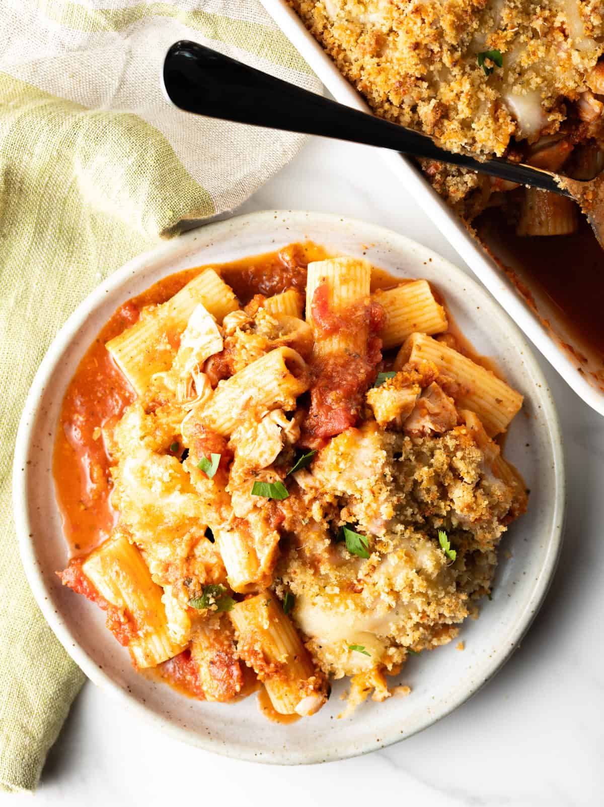 A serving of chicken parmesan casserole on a plate with a white baking dish near by.