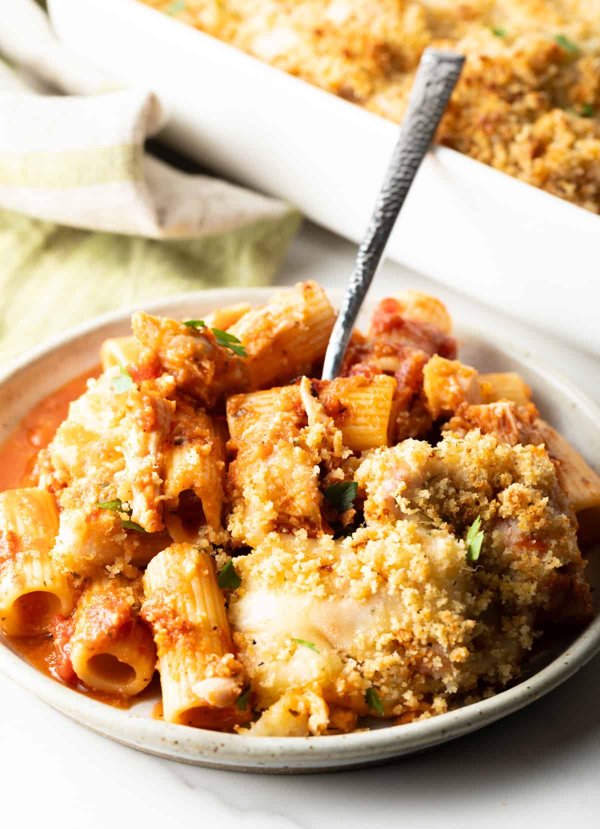 A fork taking a bite out of chicken parmesan casserole from a white plate.