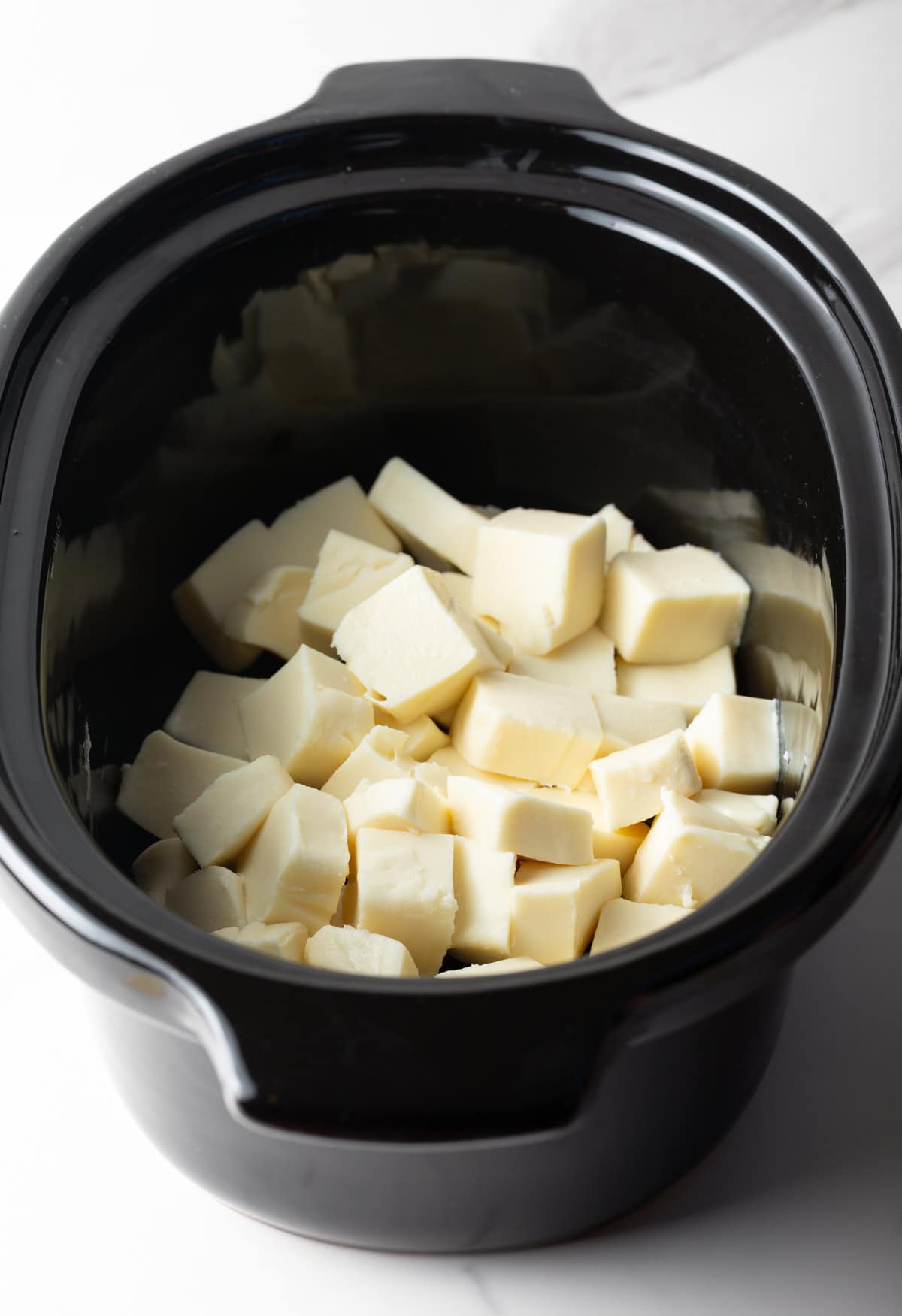 Cubed white American cheese sitting in a black crock pot.