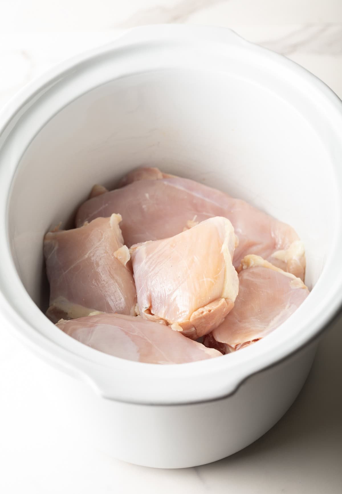 Raw chicken breasts in a white crockpot. 