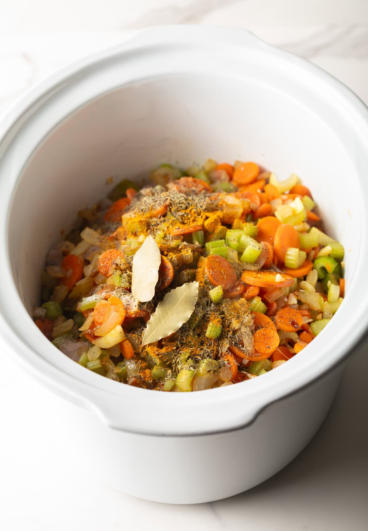 Overhead shot of vegetable mixture for crockpot chicken noodle soup sitting in a white crockpot.