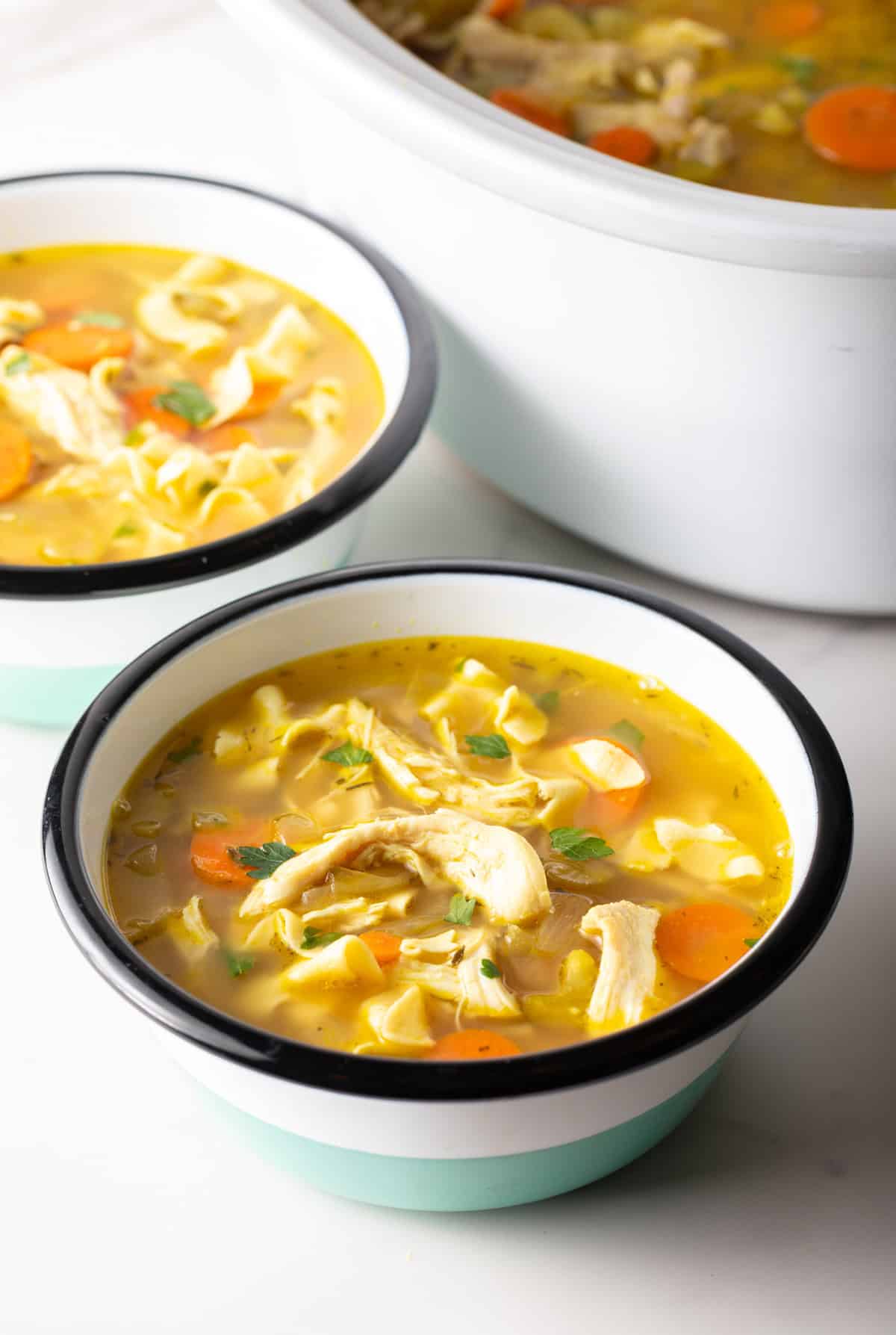 Two bowls of soup with chicken, noodles, and veggies.