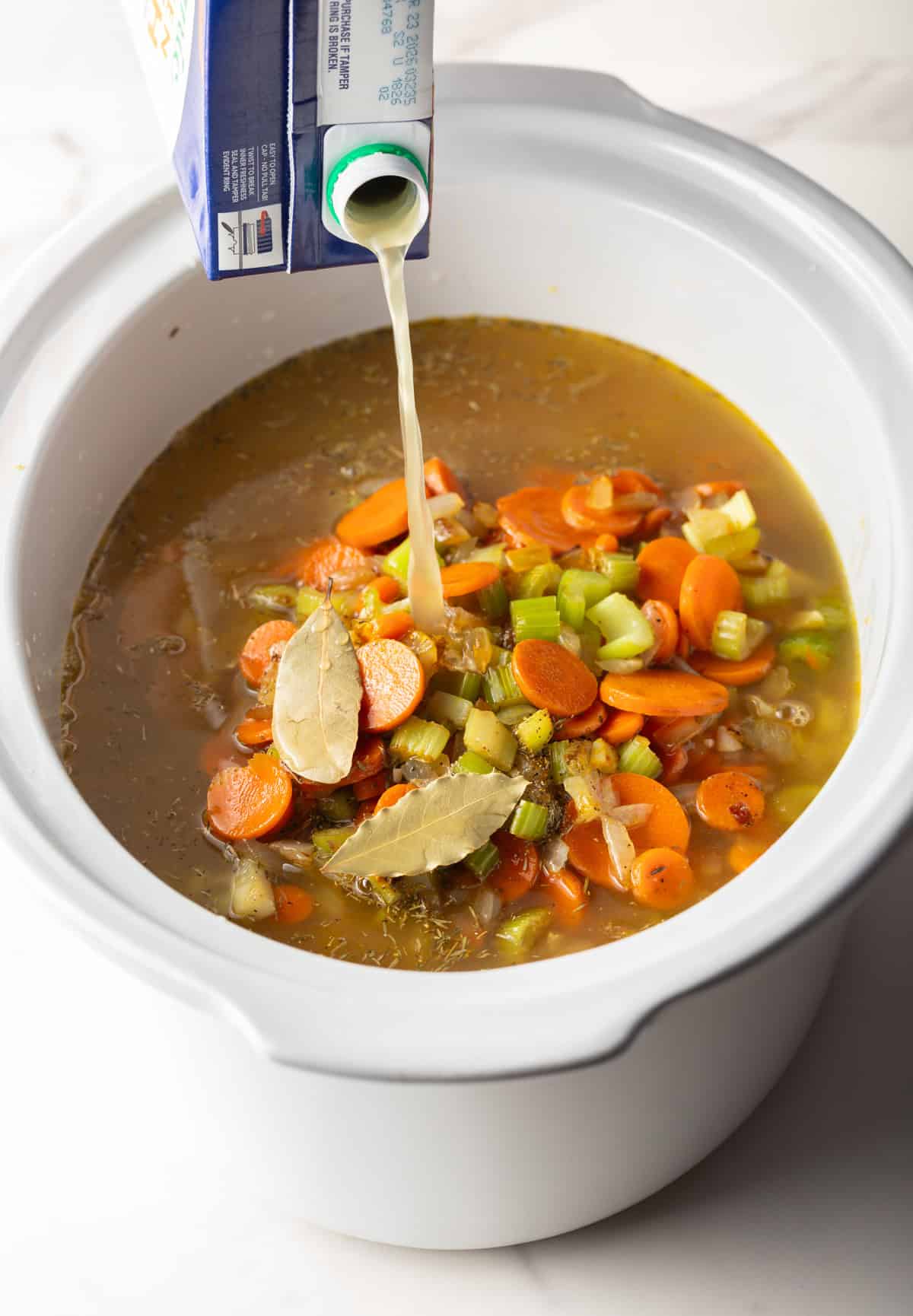 Overhead shot of chicken broth pouring over vegetable mixture for chicken noodle soup in the crockpot.