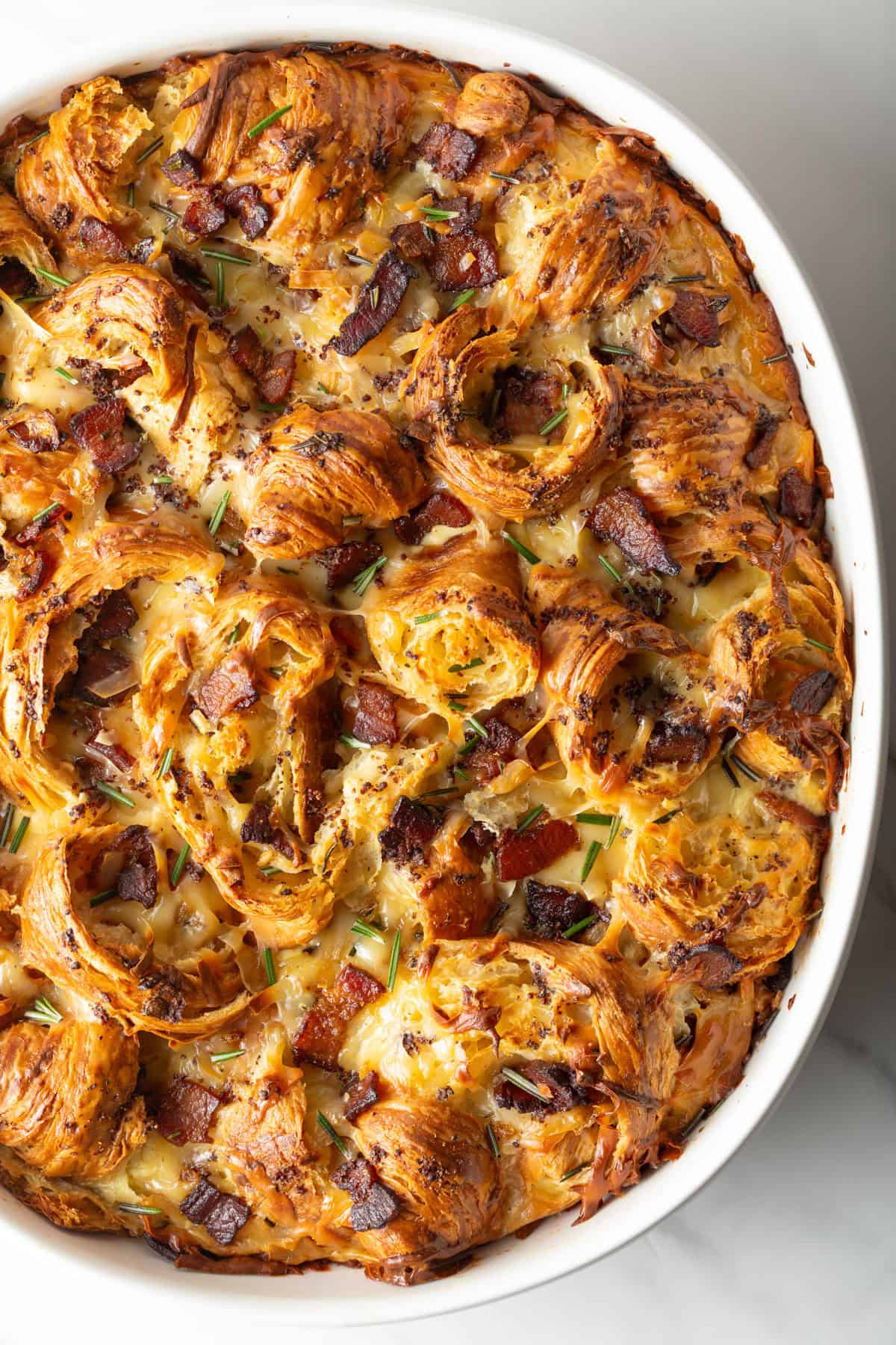 Overhead shot of croissant breakfast casserole recipe in a white baking dish, fresh from the oven.
