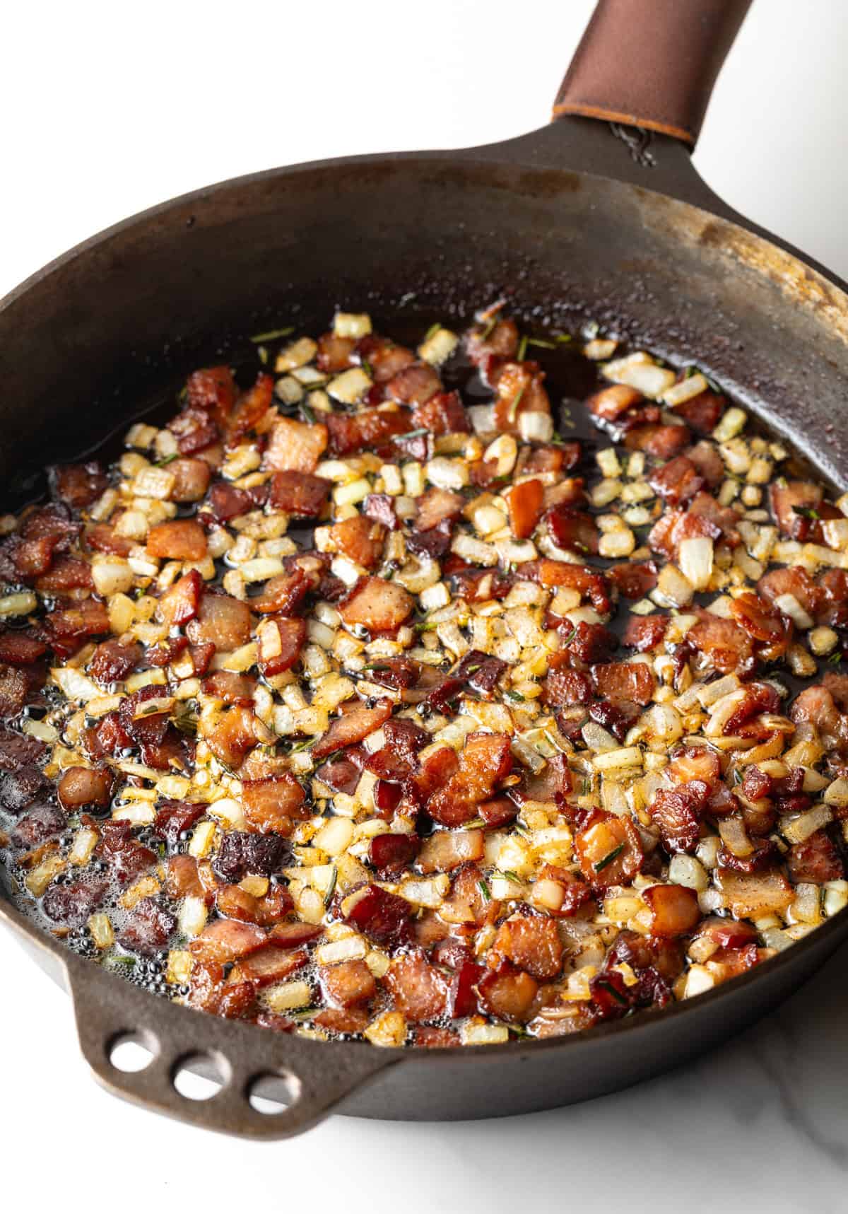 A black skillet filled with bacon and vegetables that are being sautéed. 