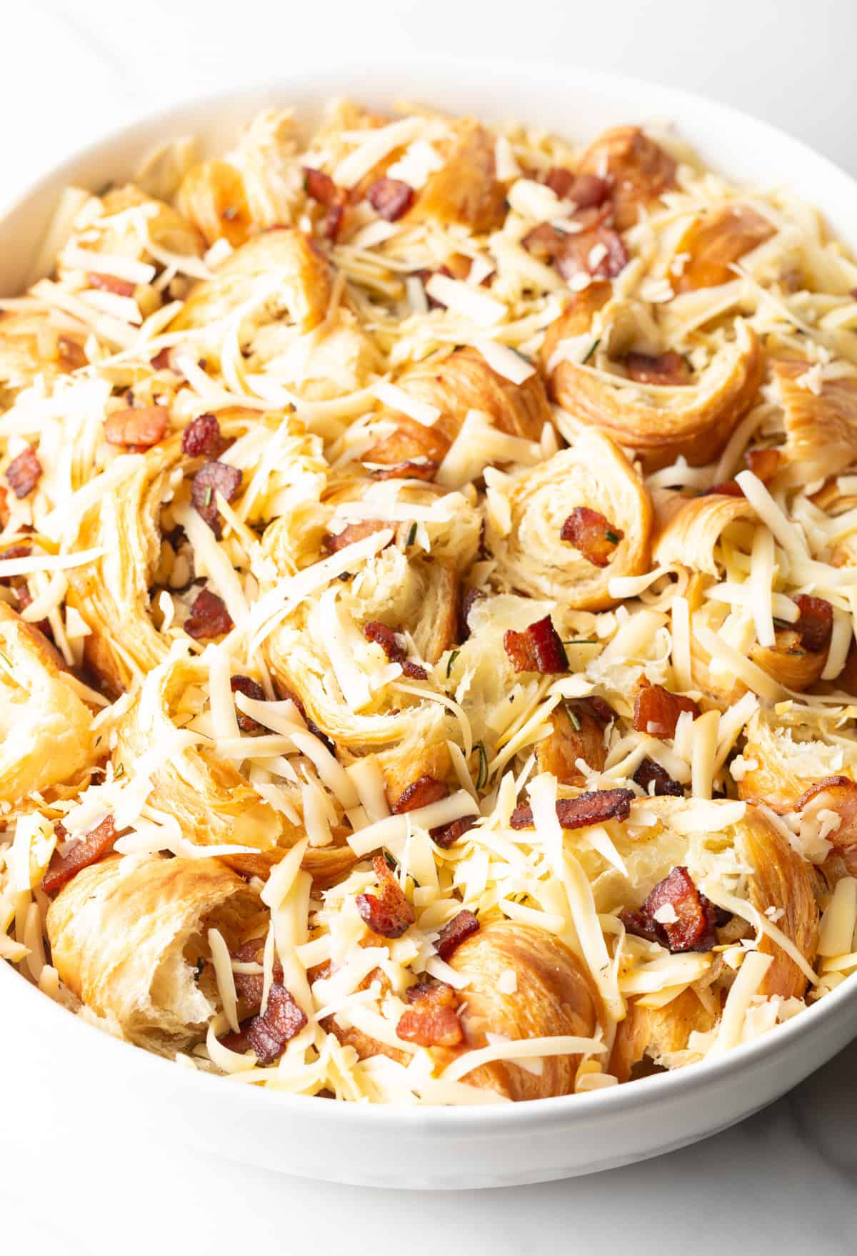 Shredded cheese is mixed into the unbaked croissant breakfast casserole.