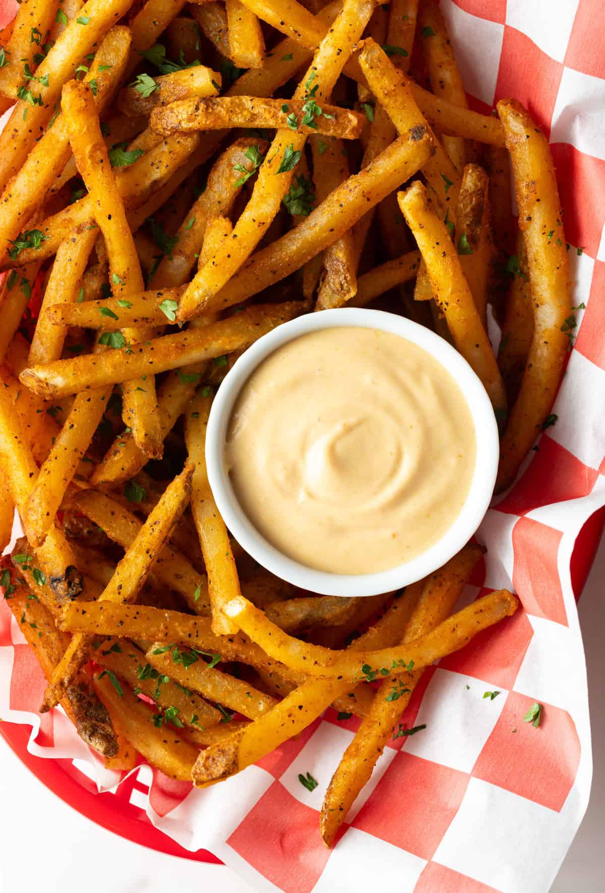 Overhead shot of a paper-lined basket of French fries surrounding a white ramekin filled with homemade French fry sauce.
