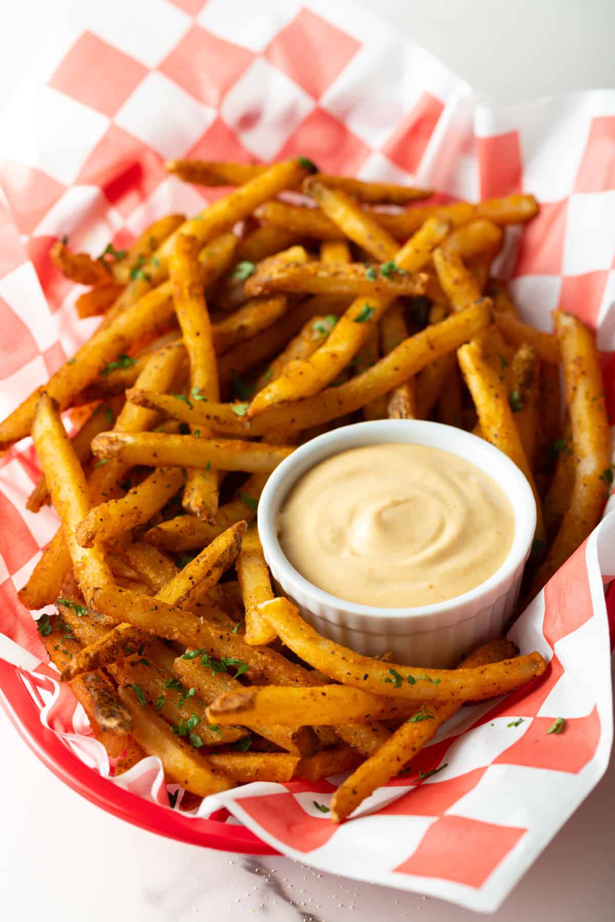 A paper-lined basket of French fries surrounding a white ramekin filled with creamy French fry sauce.