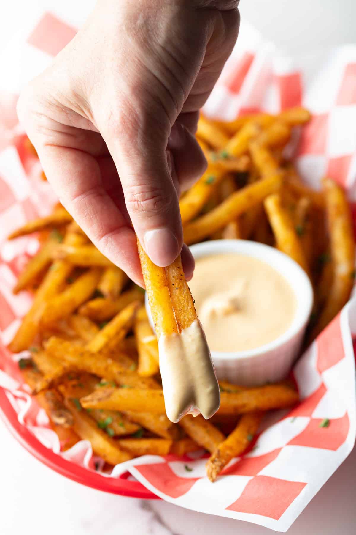 A hand holding two French fries that have been dipped in easy French fry dipping sauce.