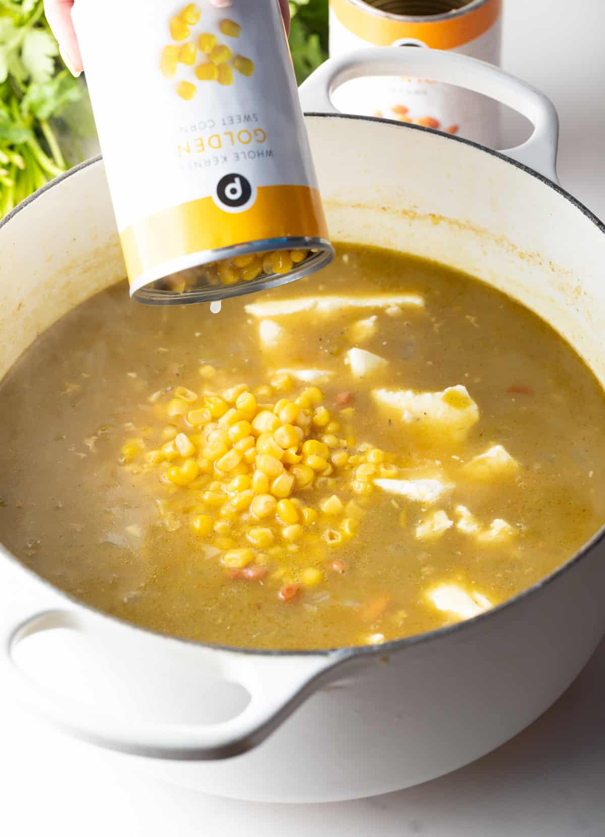 Pouring corn from a can into a large pot of chicken soup.