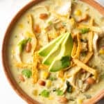 Top down view bowl of green chicken enchilada soup, topped with tortilla strips and slices of avocado.